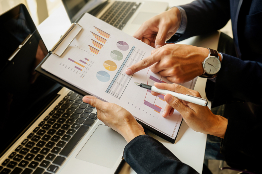 Manos de dos personas revisando un documento con gráficas de barras, circulares y tabla de datos