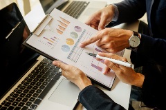 Manos de dos personas revisando un documento con gráficas de barras, circulares y tabla de datos